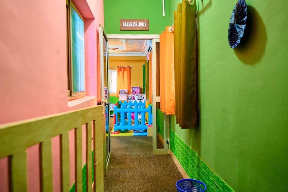 Le couloir menant à la salle de jeux, aux murs verts et roses, avec sa plaque « Salle de jeux ».