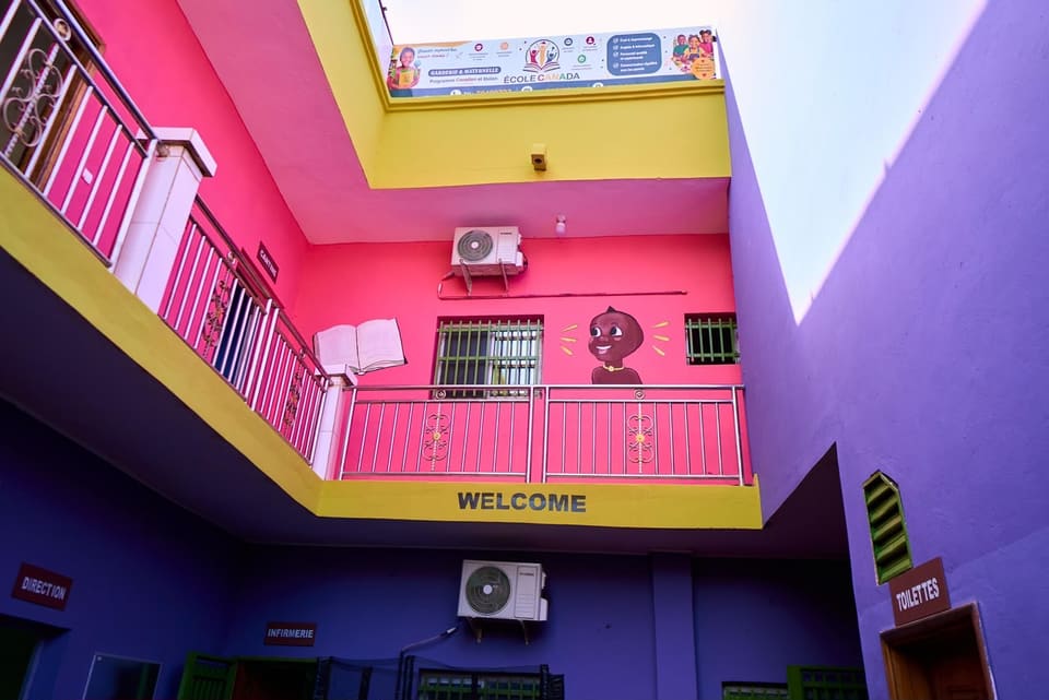 La cour intérieure de l’école vue d’en bas : balcon à balustrade, murs roses, violets et jaunes, et l’inscription « Welcome ».